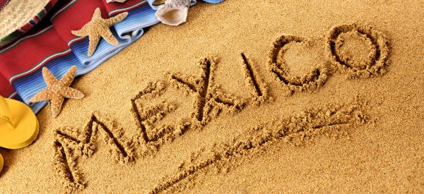 A sand writing on the beach with shoes and sandals