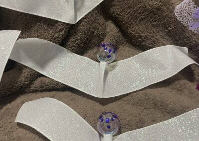 White ribbon crafts with purple bead accents.